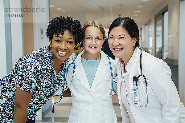 Porträt von fröhlichen Ärztinnen mit Mädchen im Laborkittel im Krankenhaus