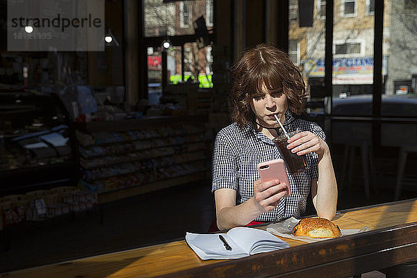 Frau trinkt Cola  während sie im Café ein Smartphone benutzt