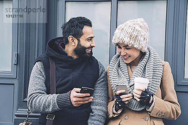 Glücklicher Mann zeigt seiner Freundin sein Handy  während er sich am Gebäude anlehnt