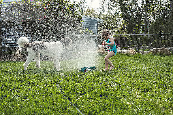 Seitenansicht von Mädchen und Hund beim Sprühen von Wasser im Hof