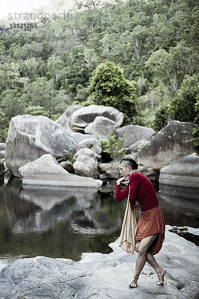 Seitenansicht einer Frau  die auf einem Felsen am See im Wald tanzt