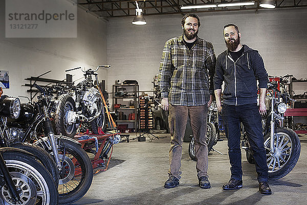 Zuversichtliche Mechaniker stehen bei Motorrädern in der Autowerkstatt