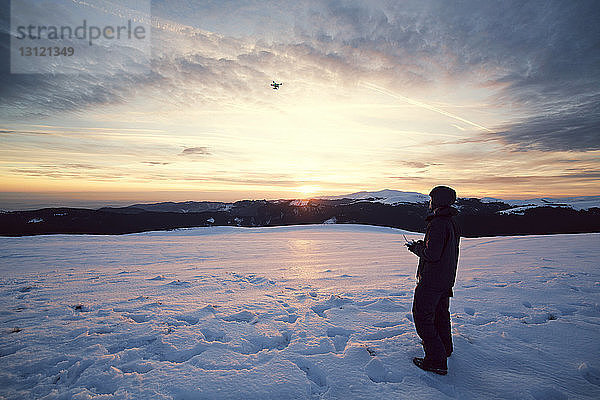 Mann fliegt Drohne am Himmel  während er auf schneebedeckten Bergen steht