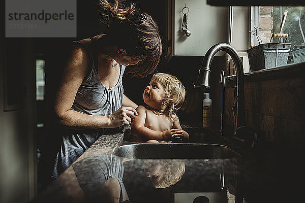 Mutter badet hemdlose Tochter zu Hause in der Küchenspüle