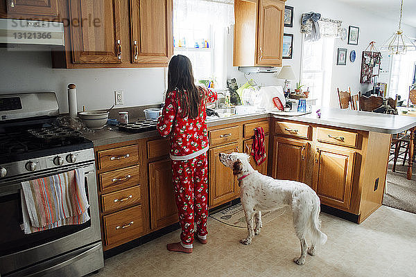 Rückansicht eines Mädchens  das Essen zubereitet  während es in der Küche beim Hund steht