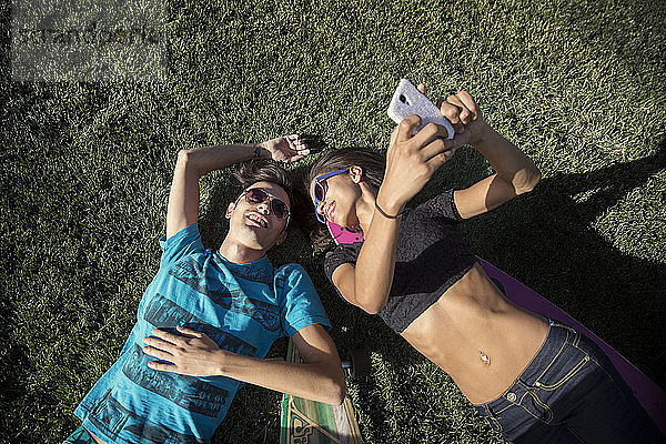 Draufsicht auf eine Frau  die sich mit einem Freund auf einem Grasfeld liegend ein Selfie nimmt
