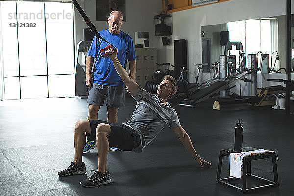 Trainer zeigt dem Kunden im Fitnessstudio eine Dehnungsübung mit Widerstandsband