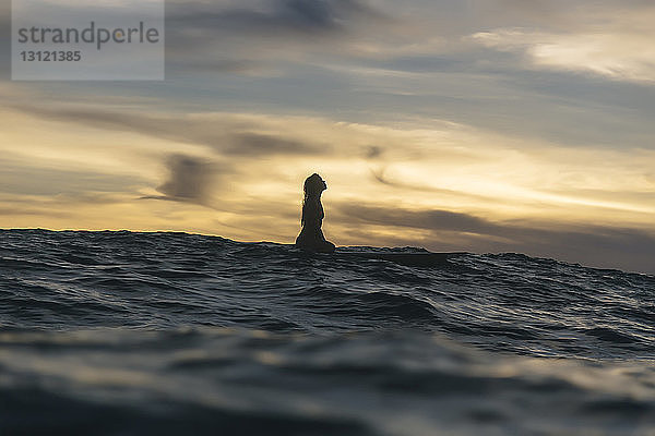 Mitteldistanzansicht der Silhouette einer jungen Frau im Meer vor bewölktem Himmel bei Sonnenuntergang