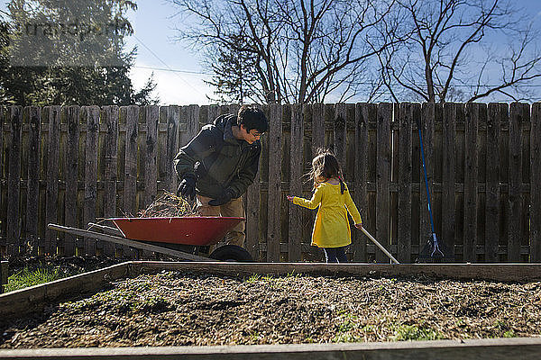 Tochter hilft Vater bei der Gartenarbeit gegen Zaun im Hinterhof