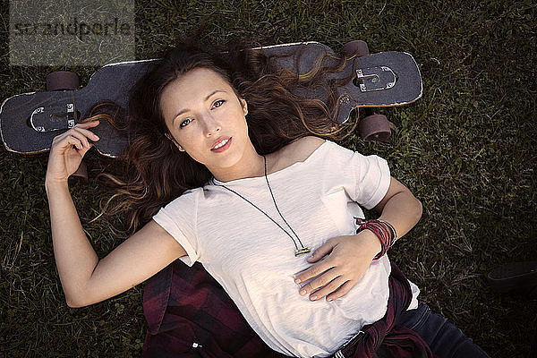 Draufsicht einer Frau  die mit dem Kopf auf einem Skateboard liegt  während sie auf einem Grasfeld liegt