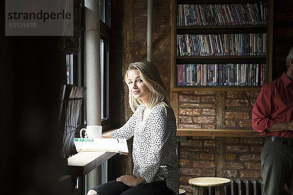 Porträt einer lächelnden Frau mit Zeitung beim Kaffeetrinken im Café
