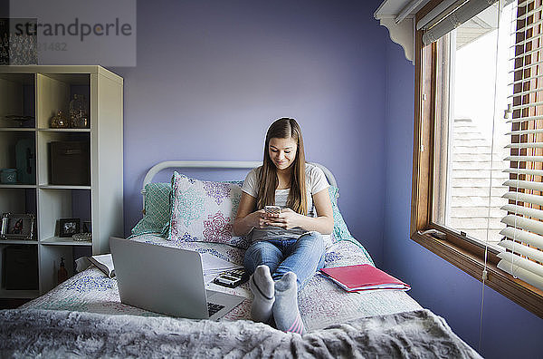 Lächelndes Mädchen benutzt Smartphone  während es zu Hause im Bett sitzt