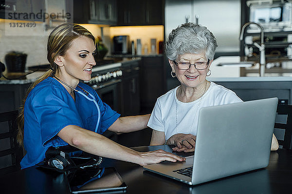 Hauspflegerin und ältere Frau schauen auf Laptop-Computer auf dem Esstisch