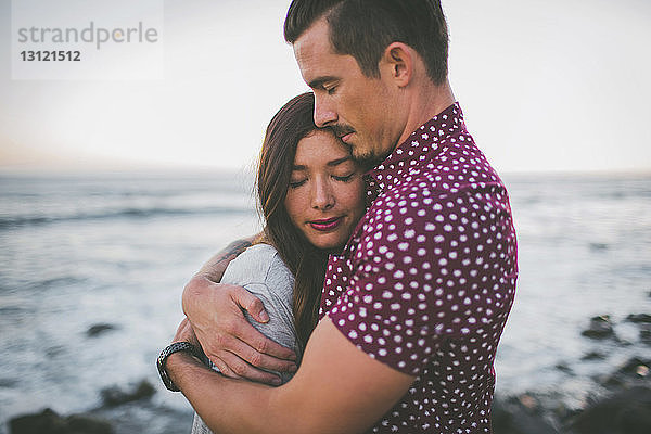 Paar umarmt sich  während es am Strand vor klarem Himmel steht