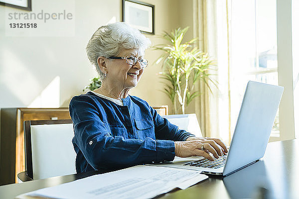 Ältere Frau lächelt  während sie zu Hause einen Laptop benutzt