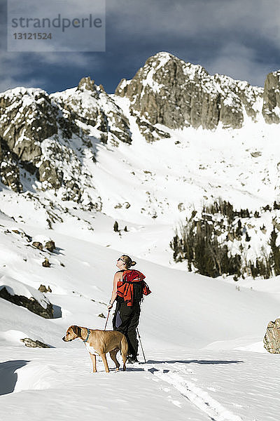 Wanderin mit Hund steht vor schneebedecktem Berg