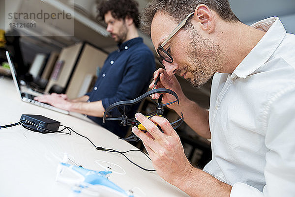 Ingenieur untersucht Drohne  während ein Mitarbeiter einen Laptop im Büro benutzt