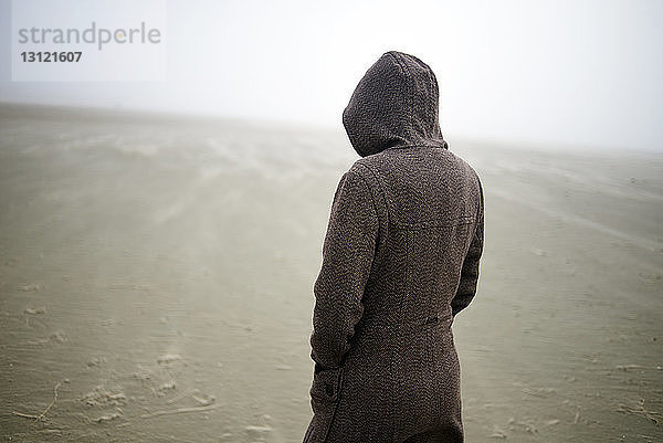 Frau mit Kapuzenmantel am Strand bei nebligem Wetter