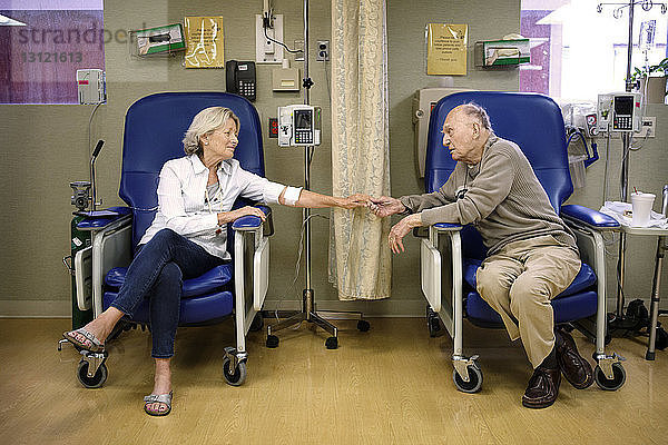Älteres Ehepaar  das im Krankenhaus auf Stühlen sitzend Händchen hält