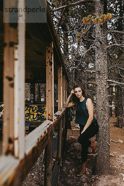 Porträt einer selbstbewussten jungen Frau  die an einem verlassenen Fahrzeug im Wald steht