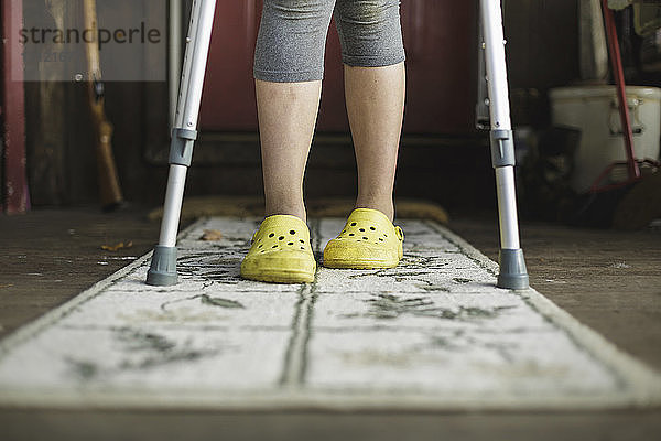 Mädchen mit Krücken steht zu Hause auf dem Teppich