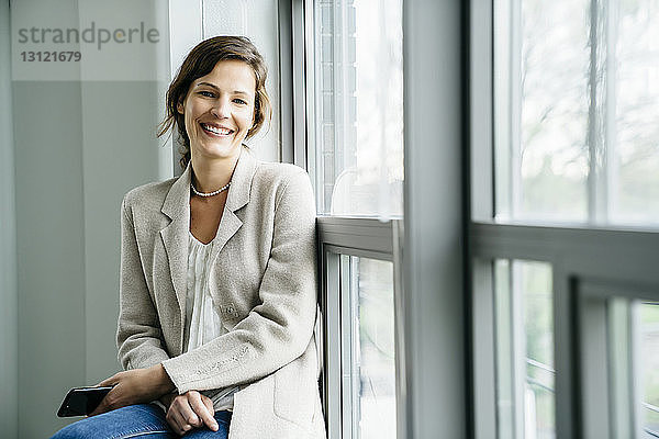 Porträt einer lächelnden Geschäftsfrau  die im Büro am Fenster sitzt