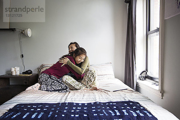 Mutter umarmt Mädchen  während sie zu Hause auf dem Bett sitzt