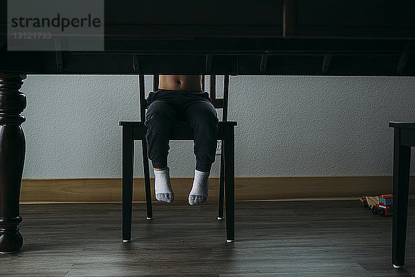 Niederer Teil eines Jungen  der zu Hause auf einem Stuhl am Tisch sitzt