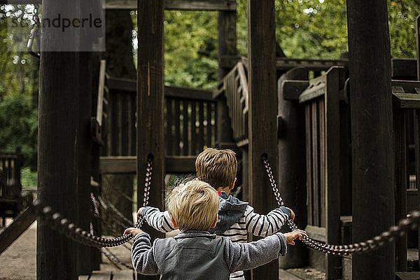 Rückansicht der Brüder  die auf dem Spielplatz eine Kette gegen die Dschungelturnhalle halten