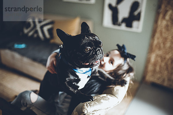 Schrägansicht eines Mädchens mit französischer Bulldogge sitzendem Sofa zu Hause