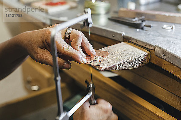 Geschnittene Hände einer Handwerkerin mit einer Handsäge bei der Arbeit am Tisch in der Werkstatt