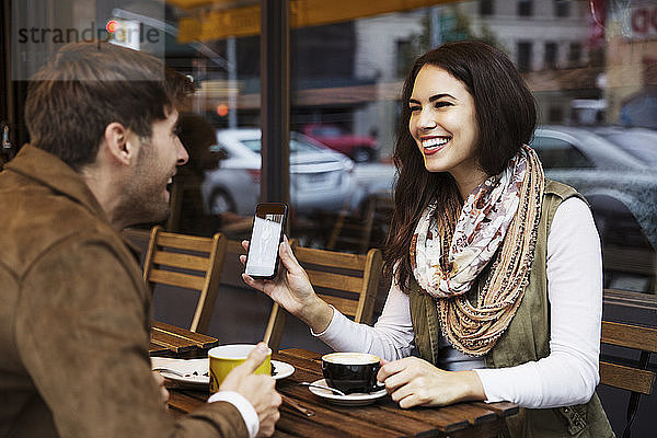 Glückliche Frau zeigt ihrem Freund ihr Handy  während sie im Café Kaffee trinkt