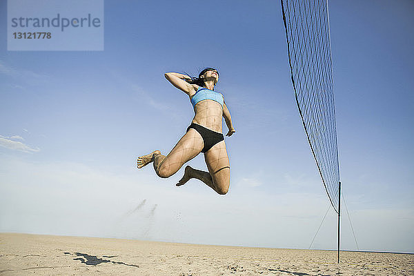 Tiefwinkelansicht einer Frau  die beim Volleyballspielen am Strand springt