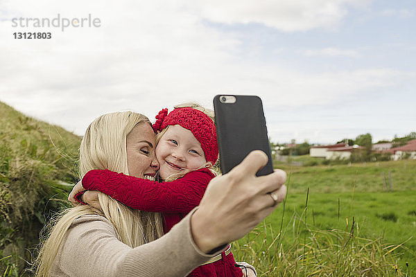 Glückliche Mutter und Tochter beim Selbstfahren mit dem Smartphone auf dem Feld