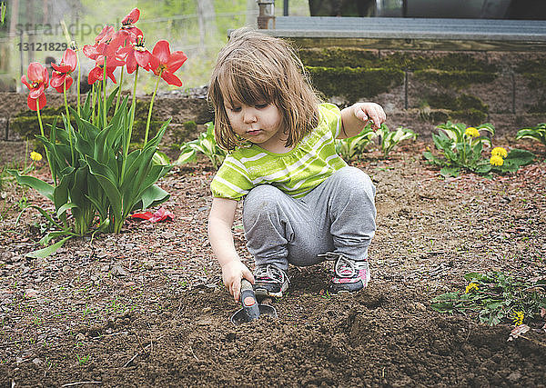 Hübsches Mädchen gräbt Erde mit der Kelle  während es im Garten kauert