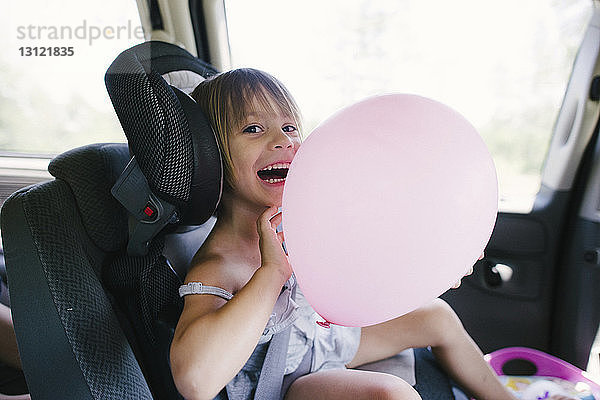 Porträt eines glücklichen Mädchens  das im Auto sitzend mit einem Ballon spielt