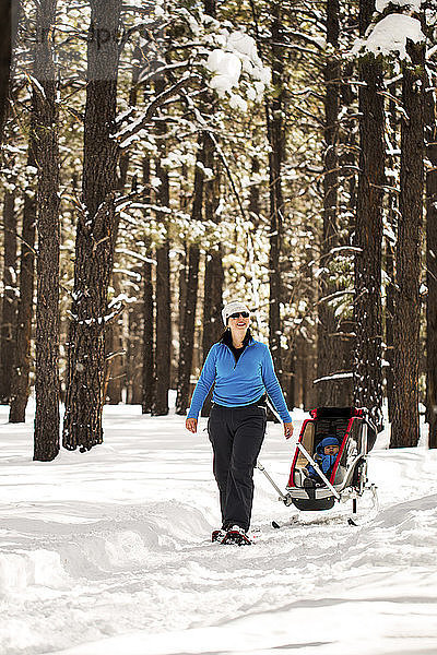Glückliche Frau mit Sohn im Schlitten auf verschneitem Feld