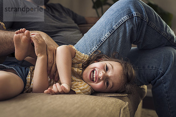 Porträt eines fröhlichen Mädchens mit Vater  der zu Hause auf dem Sofa spielt