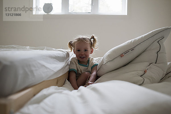 Porträt eines lächelnden Mädchens  das zu Hause am Bett auf einer Bettdecke sitzt