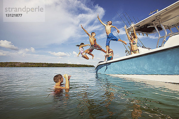 Kinder  die auf See vom Boot gegen den Himmel springen