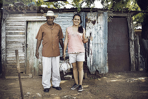 Porträt einer Frau mit einem Vater  der Fische hält  während er vor einem alten Haus steht