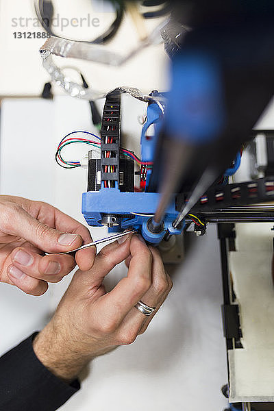 Abgetrennte Hände eines Ingenieurs  der einen 3D-Drucker auf einem Tisch im Büro befestigt