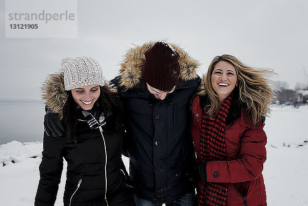 Glückliche Freunde stehen auf schneebedecktem Feld vor wolkigem Himmel