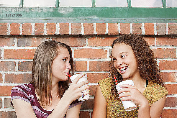 Freunde genießen ein Getränk  während sie an einer Ziegelmauer sitzen