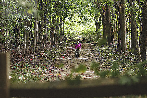 Junge in voller Länge mit einem Buch auf einem Spazierweg zwischen Bäumen im Wald