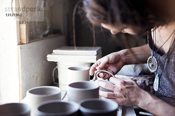 Beschnittenes Bild eines Künstlers  der in einem Workshop eine Tasse prüft