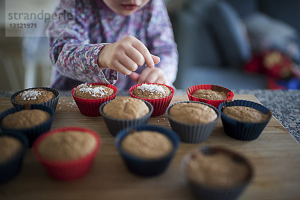 Mitschnitt eines Mädchens  das zu Hause Muffins auf einem Holztisch garniert