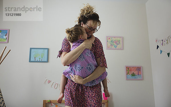 Niedrigwinkelansicht einer glücklichen Mutter  die ihre Tochter umarmt  während sie zu Hause an der Wand steht