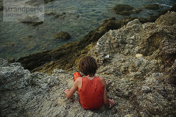 Hochwinkelaufnahme eines Jungen  der auf Felsen im Meer sitzt