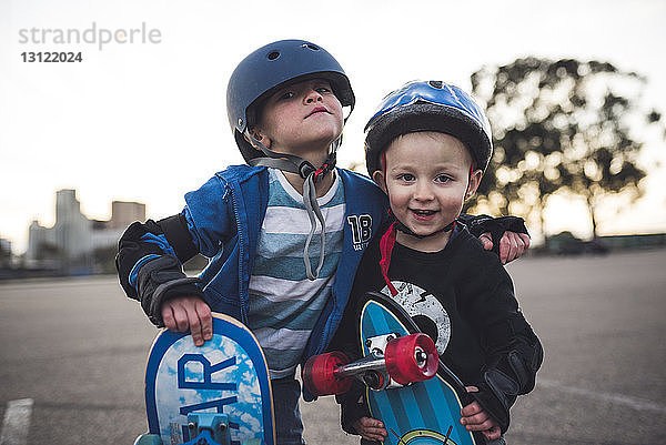 Porträt von niedlichen Jungen  die mit Skateboard auf dem Feld vor klarem Himmel stehen